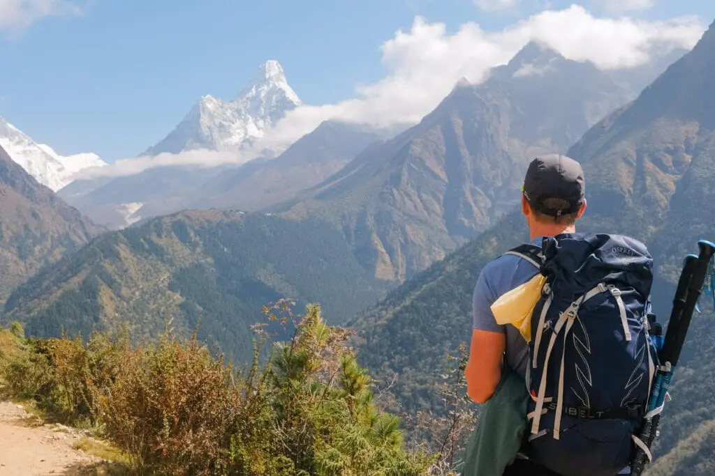 A trekker with a rucksack looking out at a panorama of mountains in the Khumbu region, Nepal