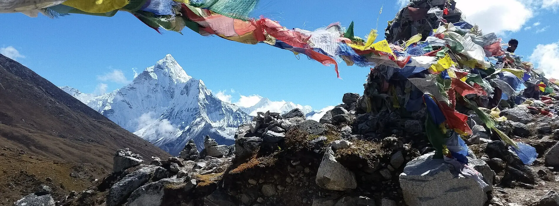 Snowcapped Himalayan mountain with colourful prayer flags fluttering in the foreground under clear blue skies.