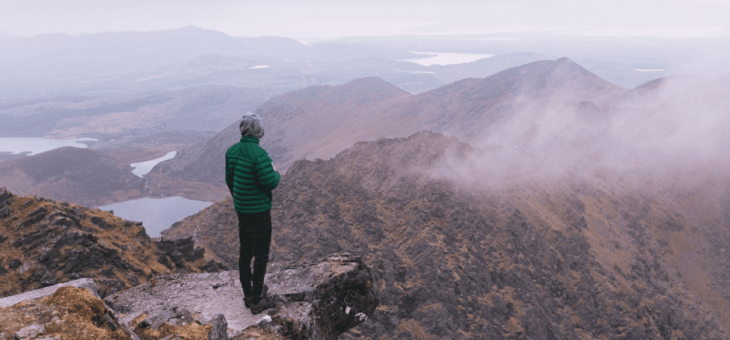 A hiker holding a cup of coffee overlooking hills shrouded in cloud in Kerry, Ireland