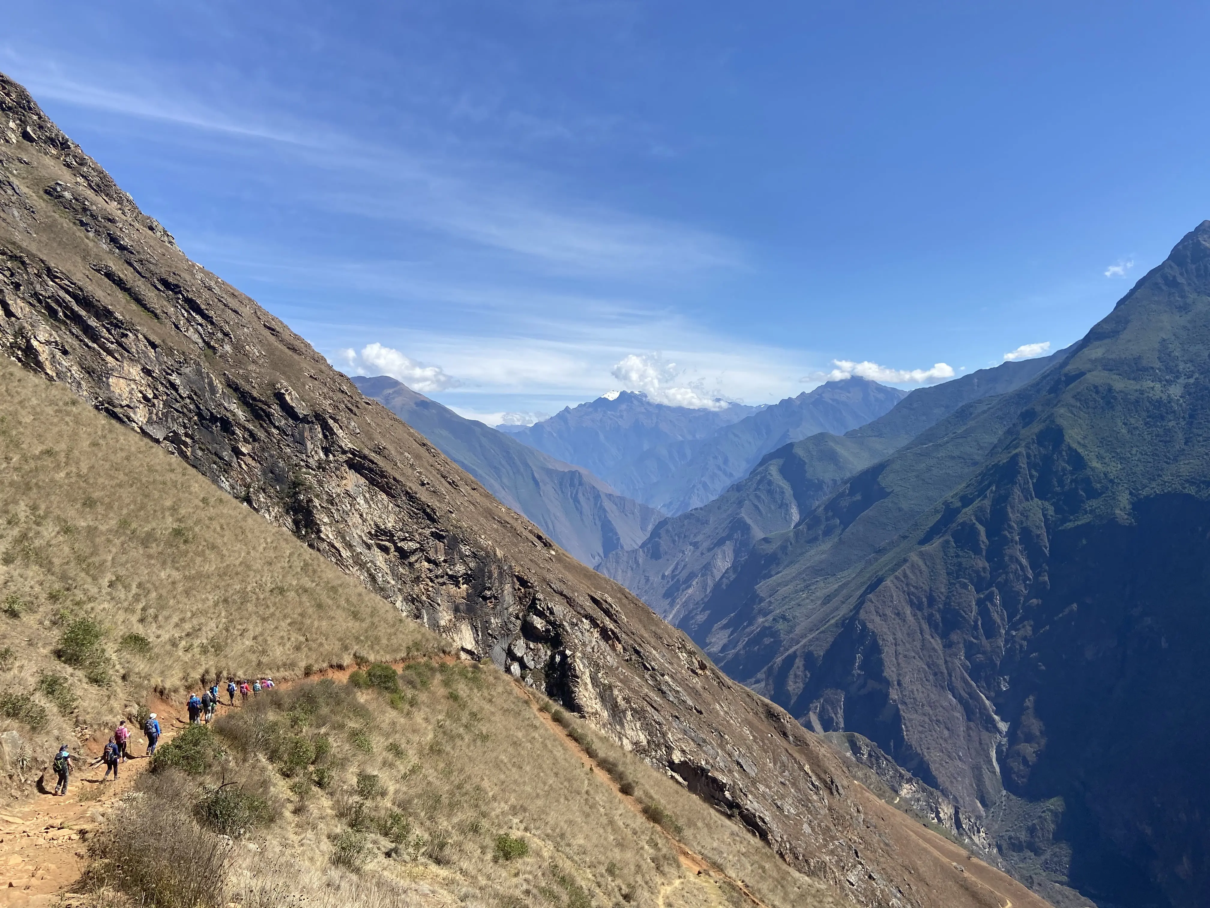 A group of hikers in single file looking tiny surrounded by imposing Andes in Peru on their way to the top of Machu Picchu