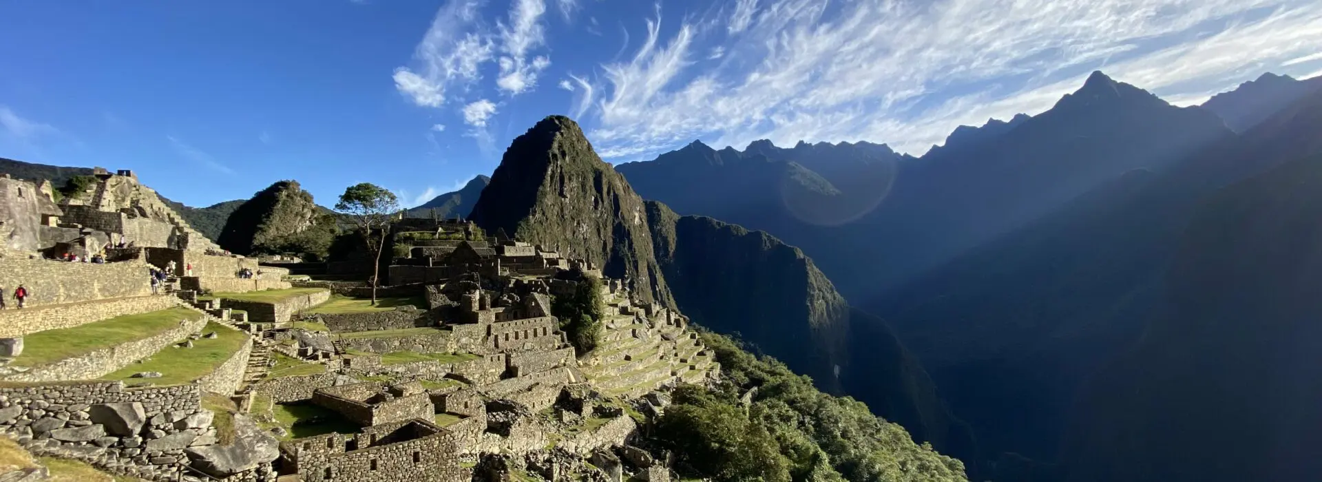 Machu Picchu site bathed in sunshine with some Inkan terraces visible and Huayna Picchu Mountain in the background