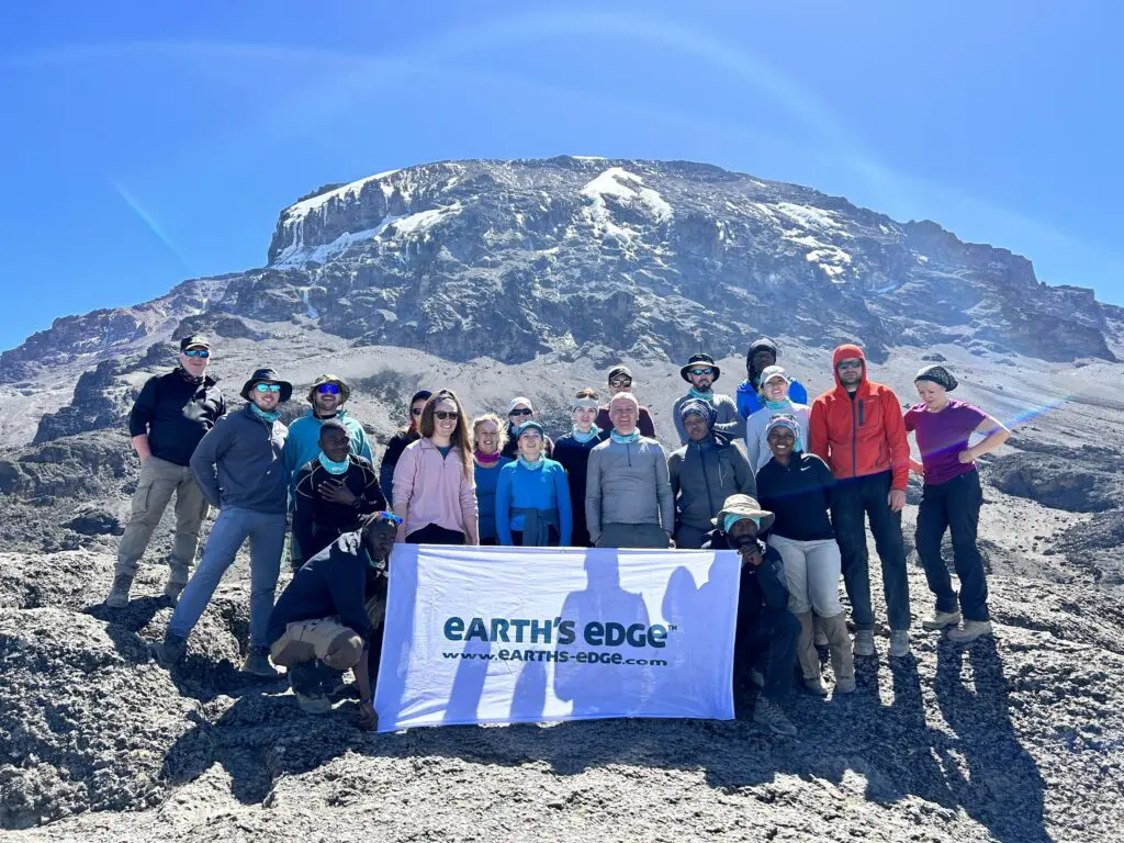 An Earth's Edge group with Mount Kilimanjaro's Uhuru Peak behind them, holding an Earth's Edge banner