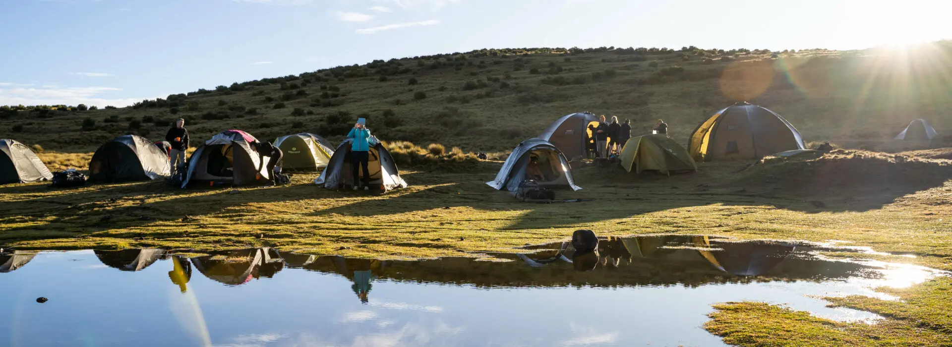 Tents bathed in sunshine set up along the lush lakefront on the Mt Kenya Tri Adventure