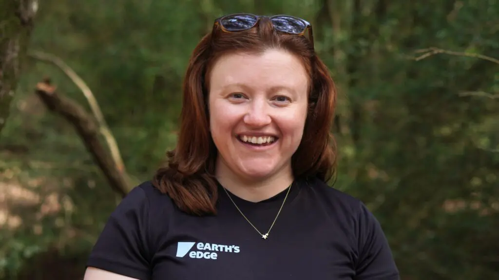 Ciara, from the Earth's Edge team, posing for a photo in front of trees.