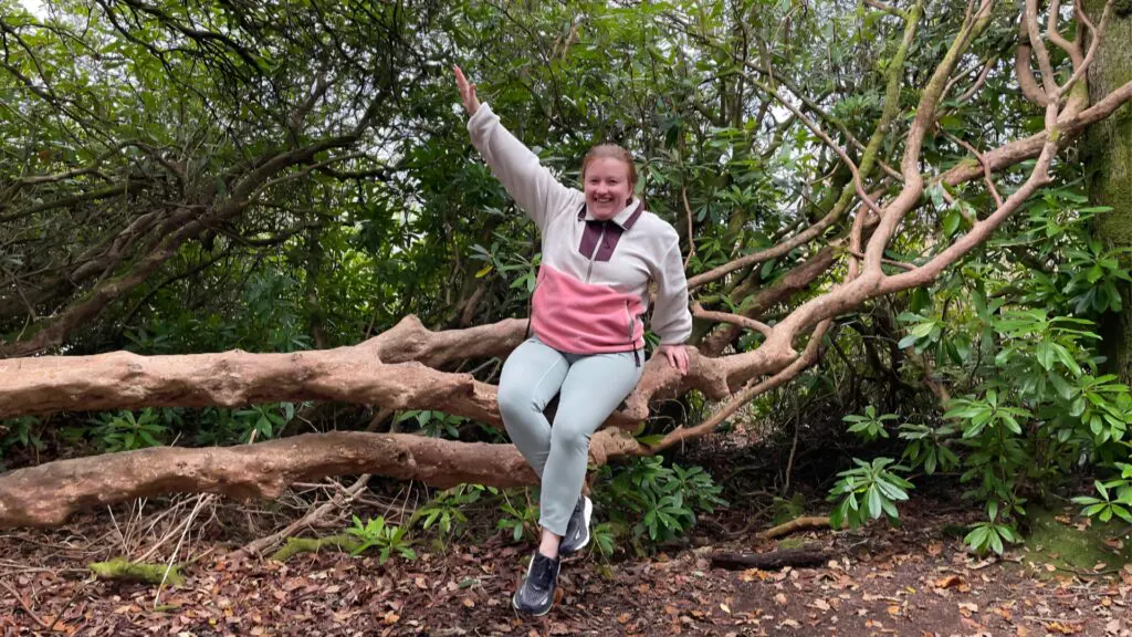 Ciara from Earth's Edge sitting on a tree branch and waving to the camera