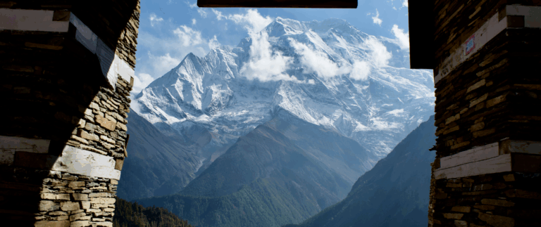 A mountain view on the Annapurna Circuit via Nar and Kang La, Nepal framed through a gap in a stone wall