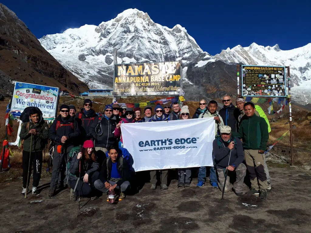 Earth's Edge trekkers and expedition team at Annapurna Base Camp, with snow-capped peaks visible in the background, Nepal