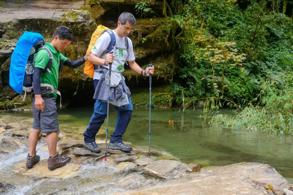 A trekker being assisted crossing a river by a Sherpa guide on the trek to Annapurna Base Camp, Nepal