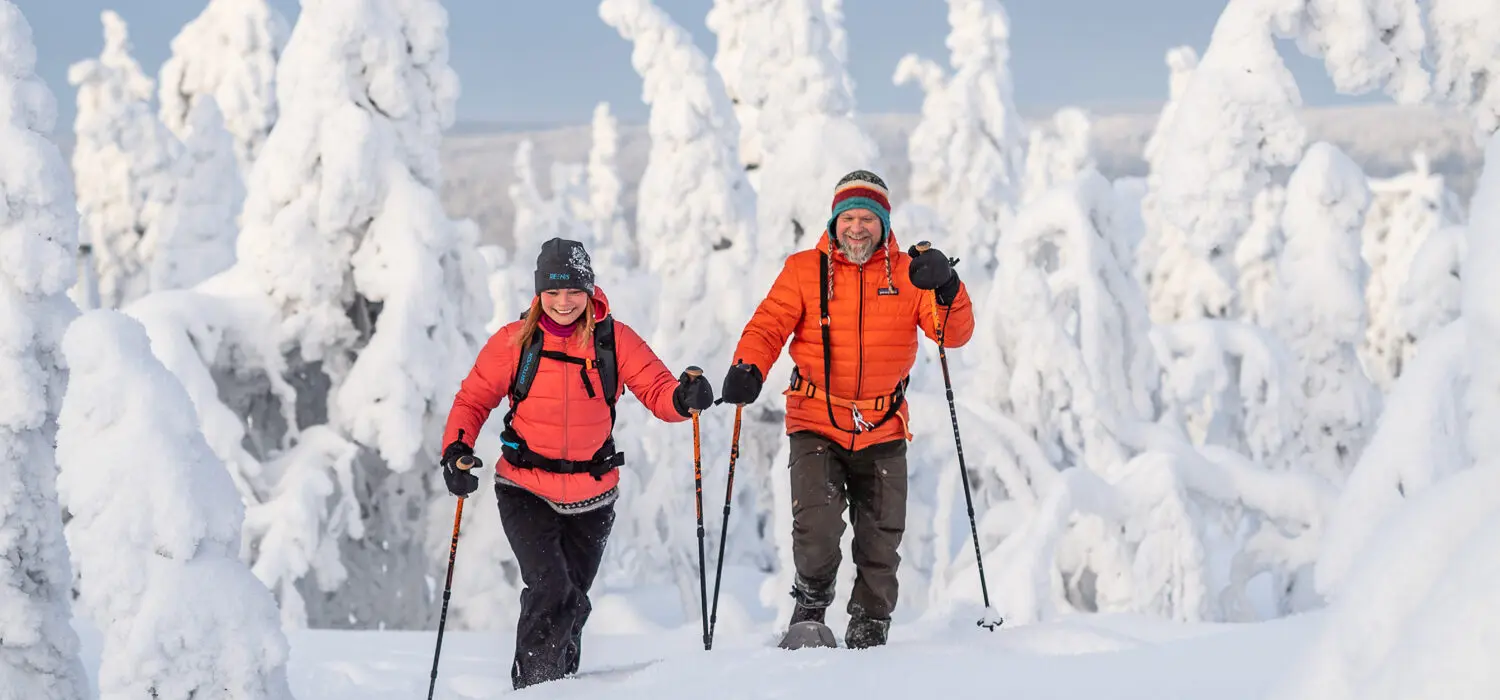 Two people snowshoeing in Arctic Finland, surrounded by snow-covered trees