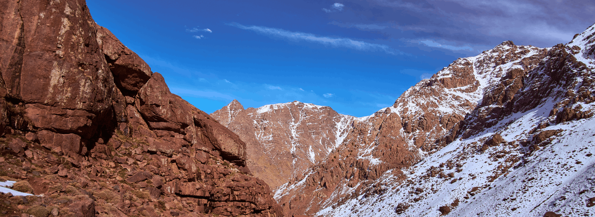 Trekker approaching Mount Toubkal through a dramatic Atlas Mountain valley with snow-covered slopes