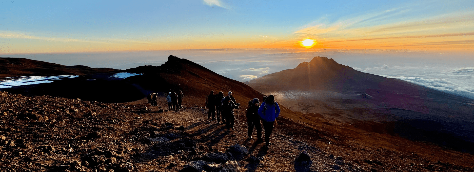 Hikers ascending Kilimanjaro as the sun rises behind them