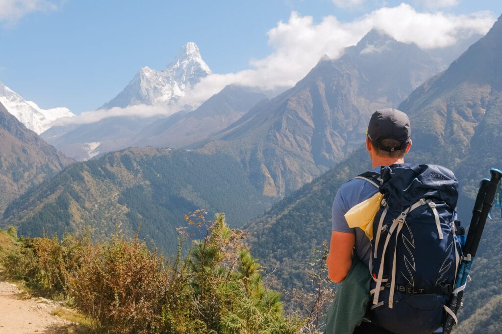 A trekker with a rucksack looking out at a panorama of mountains in the Khumbu region, Nepal