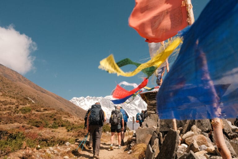 Trekkers along the route to Everest Base Camp in Nepal's Khumbu region on a clear day. Prayer flags line their path.