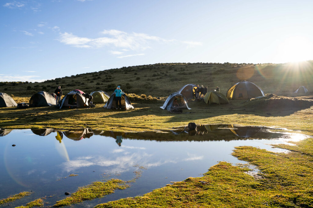 Trekkers camping beside a reflective lake on a sunny day, Kenya