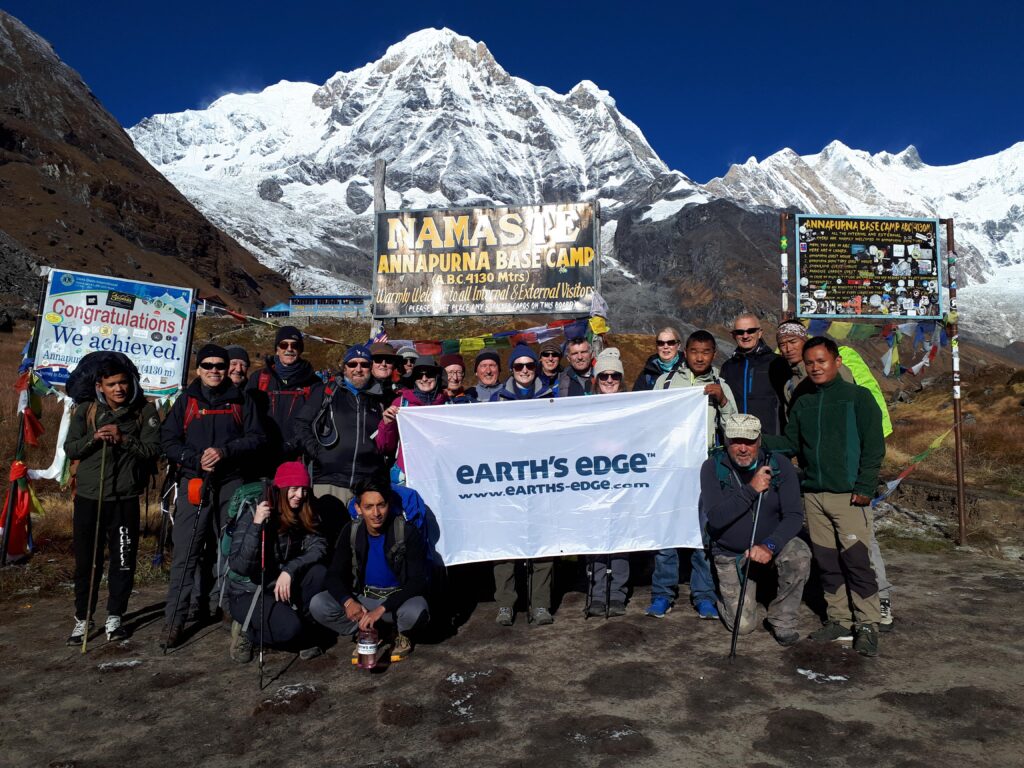 Earth's Edge trekkers and expedition team at Annapurna Base Camp, with snow-capped peaks visible in the background, Nepal