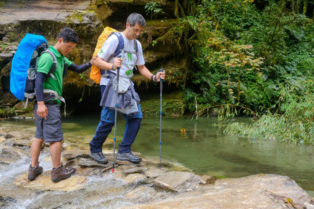 A trekker being assisted crossing a river by a Sherpa guide on the trek to Annapurna Base Camp, Nepal
