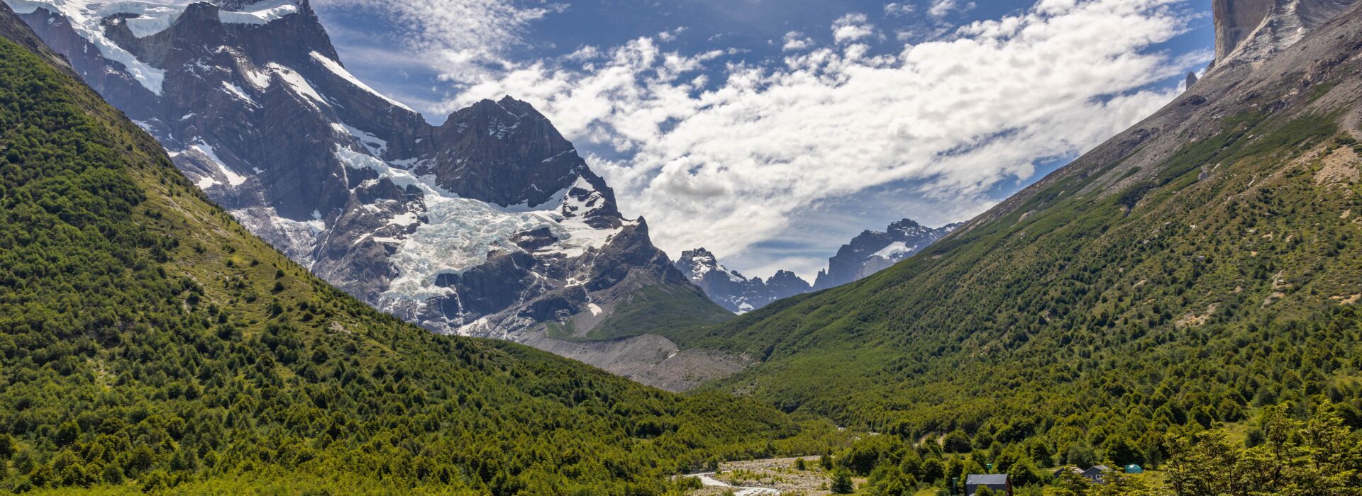 Panoramic view of a glacier descending between rugged peaks into a lush green valley in Torres del Paine National Park, Patagonia.