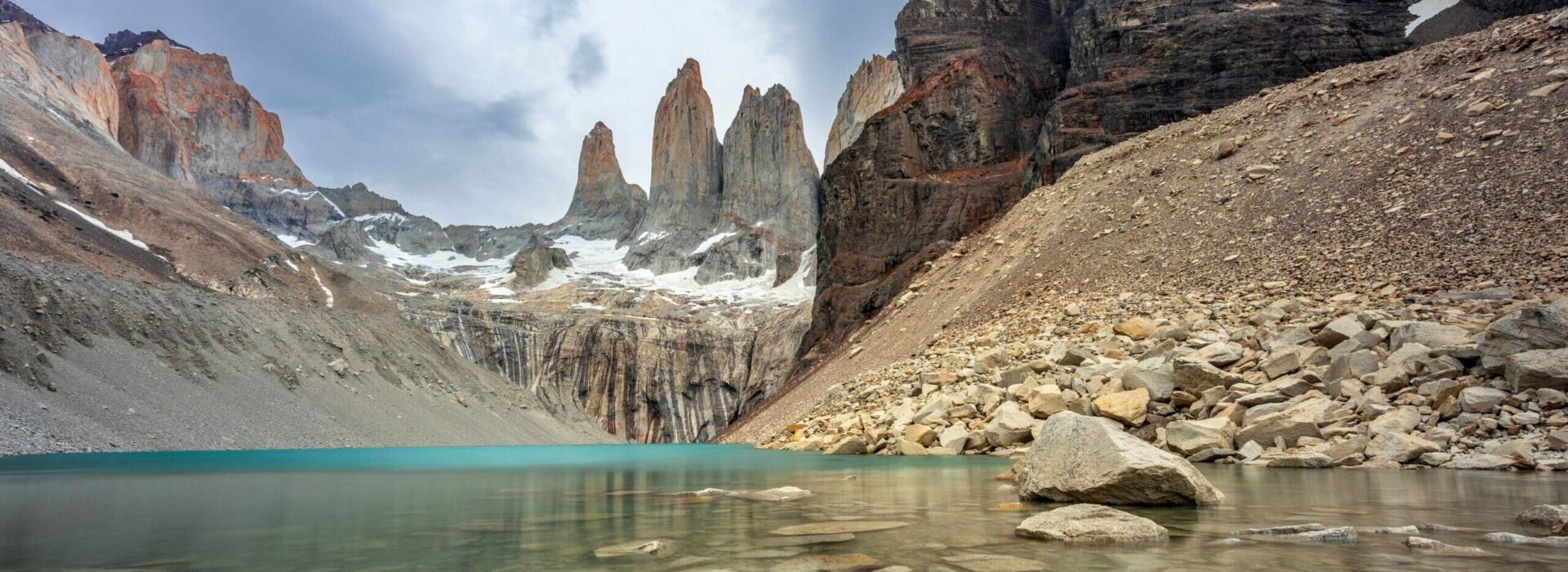 Turquoise glacial lake at the base of the granite towers in Torres del Paine National Park, Chile, viewed from the “O Circuit” trek in Patagonia.