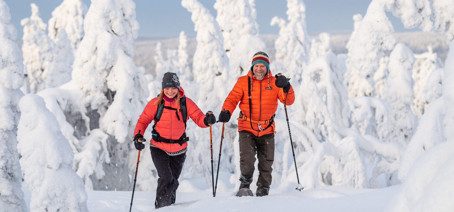 Two people snowshoeing in Arctic Finland, surrounded by snow-covered trees